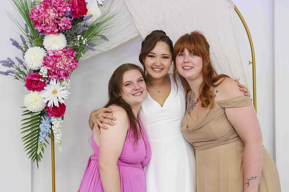 La mariée entourée de deux proches devant un décor fleuri
