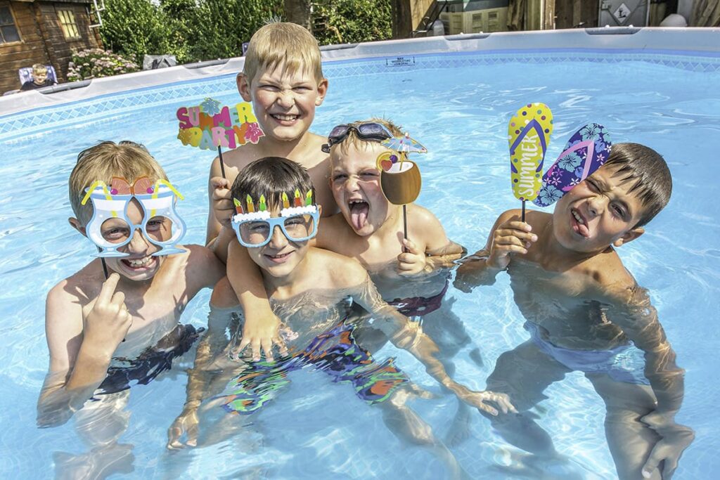 Cinq enfants souriants dans une piscine, avec des accessoires de fête.