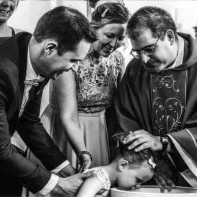 bapteme-enfant-benit-eglise-amiens Prêtre bénissant un enfant entouré de sa famille pendant un baptême à Amiens